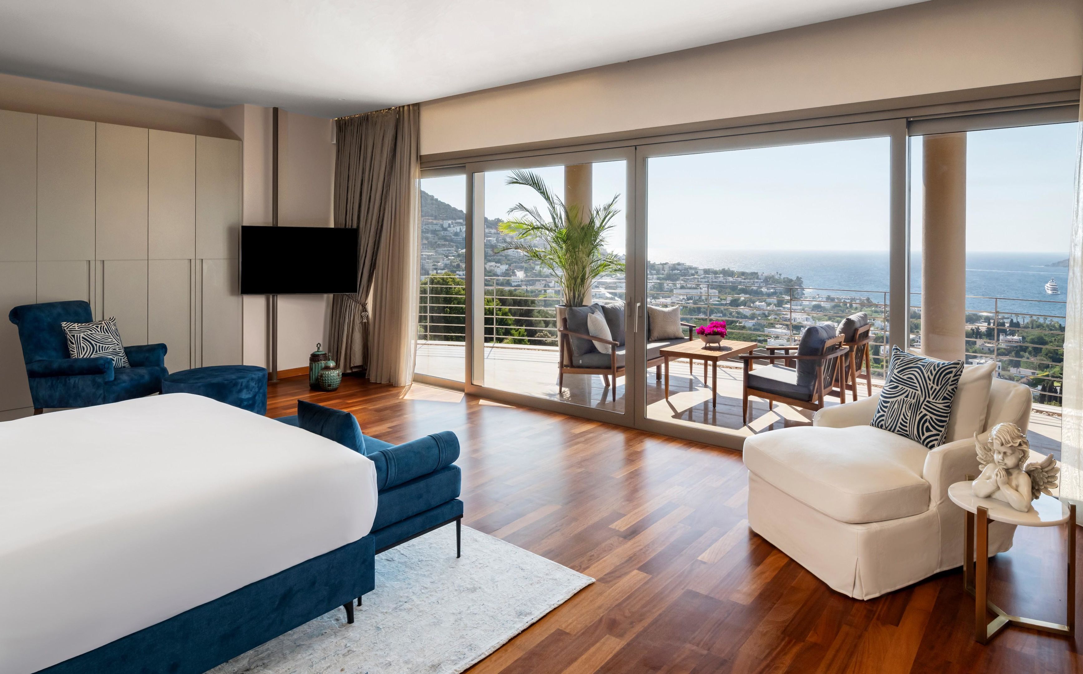 A modern hotel room with a large bed, a seating area with a view, and a balcony overlooking the city.