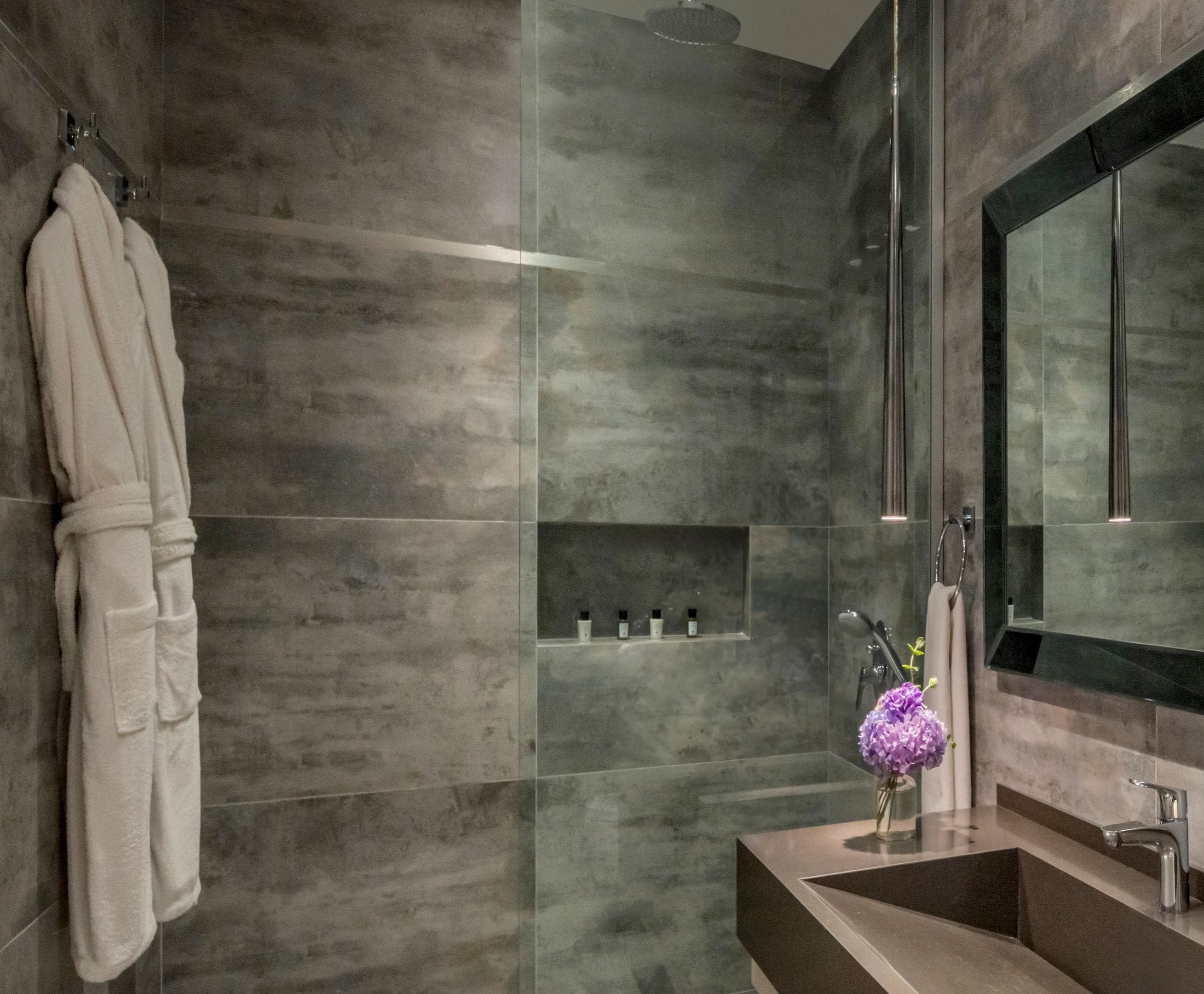 Une salle de bain moderne avec un grand miroir, une douche en verre et un meuble-lavabo agrémenté d’un vase de fleurs.