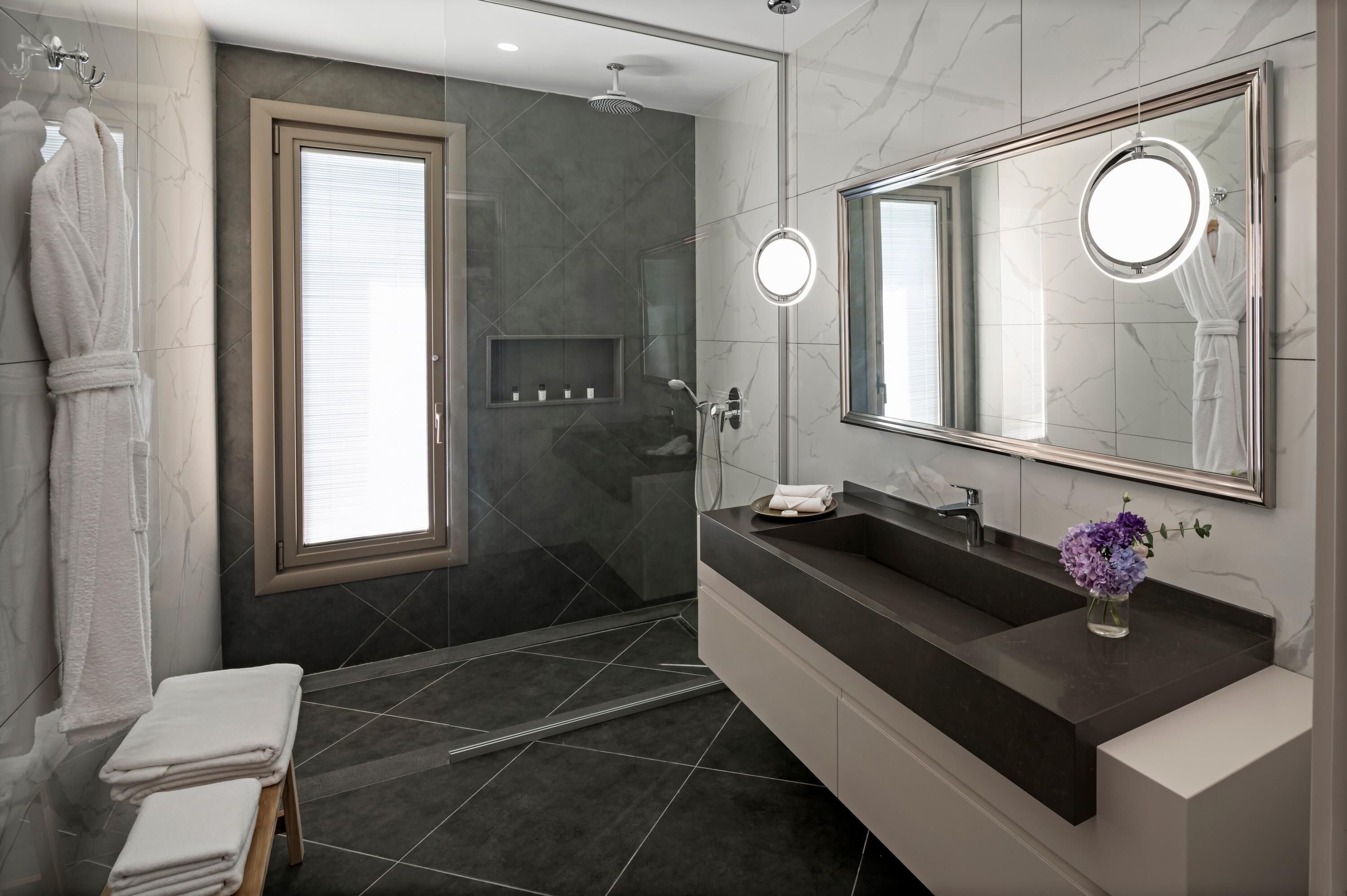 Un baño moderno con un espejo grande, un tocador con encimera oscura y una zona de ducha.