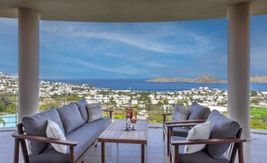 Un balcón con vista a un pueblo costero, una mesa con vasos y dos sofás.