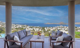 Un balcón con vista a un pueblo costero, una mesa con vasos y dos sofás.