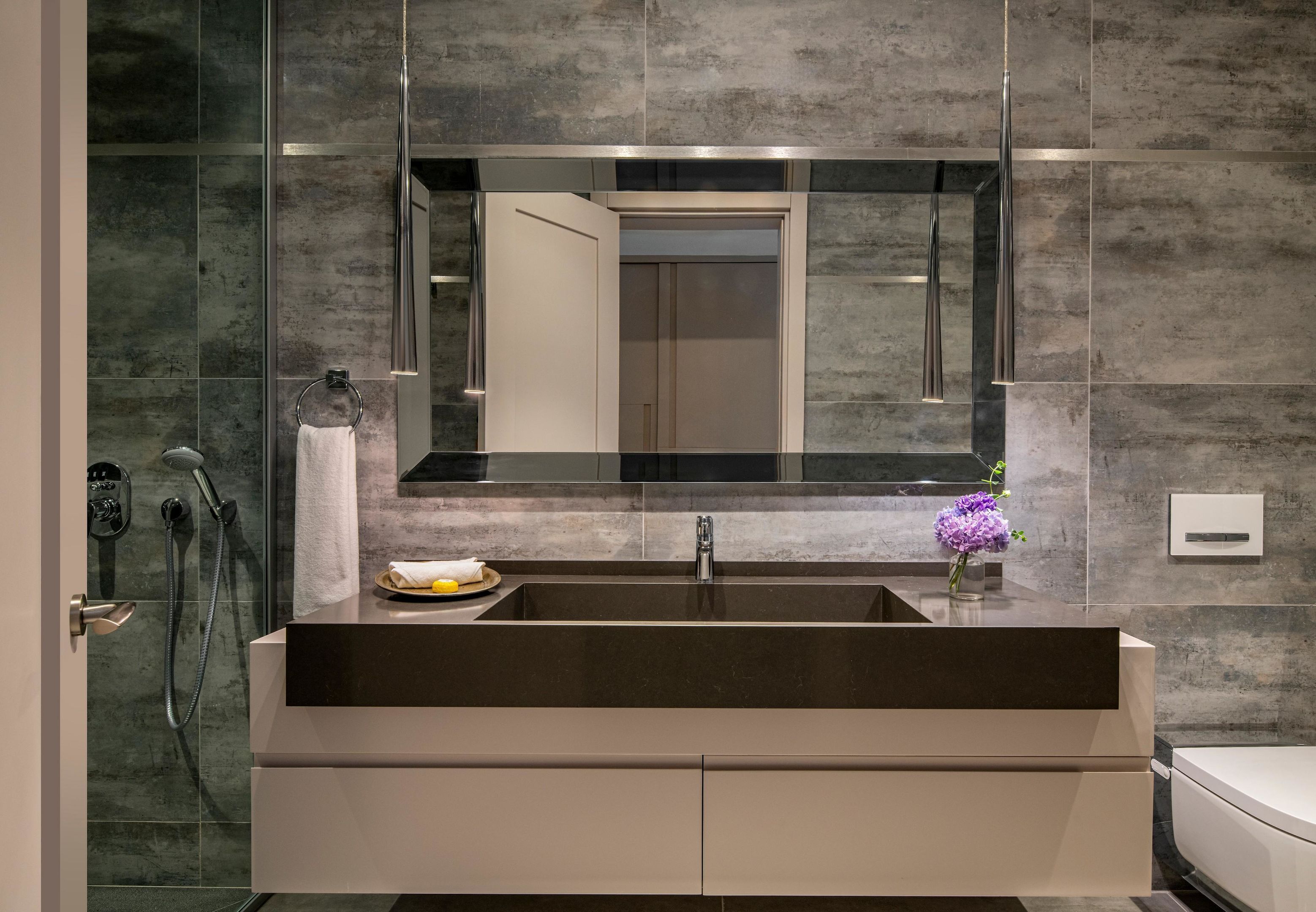 Un baño moderno con un espejo grande, un lavamanos y una ducha.