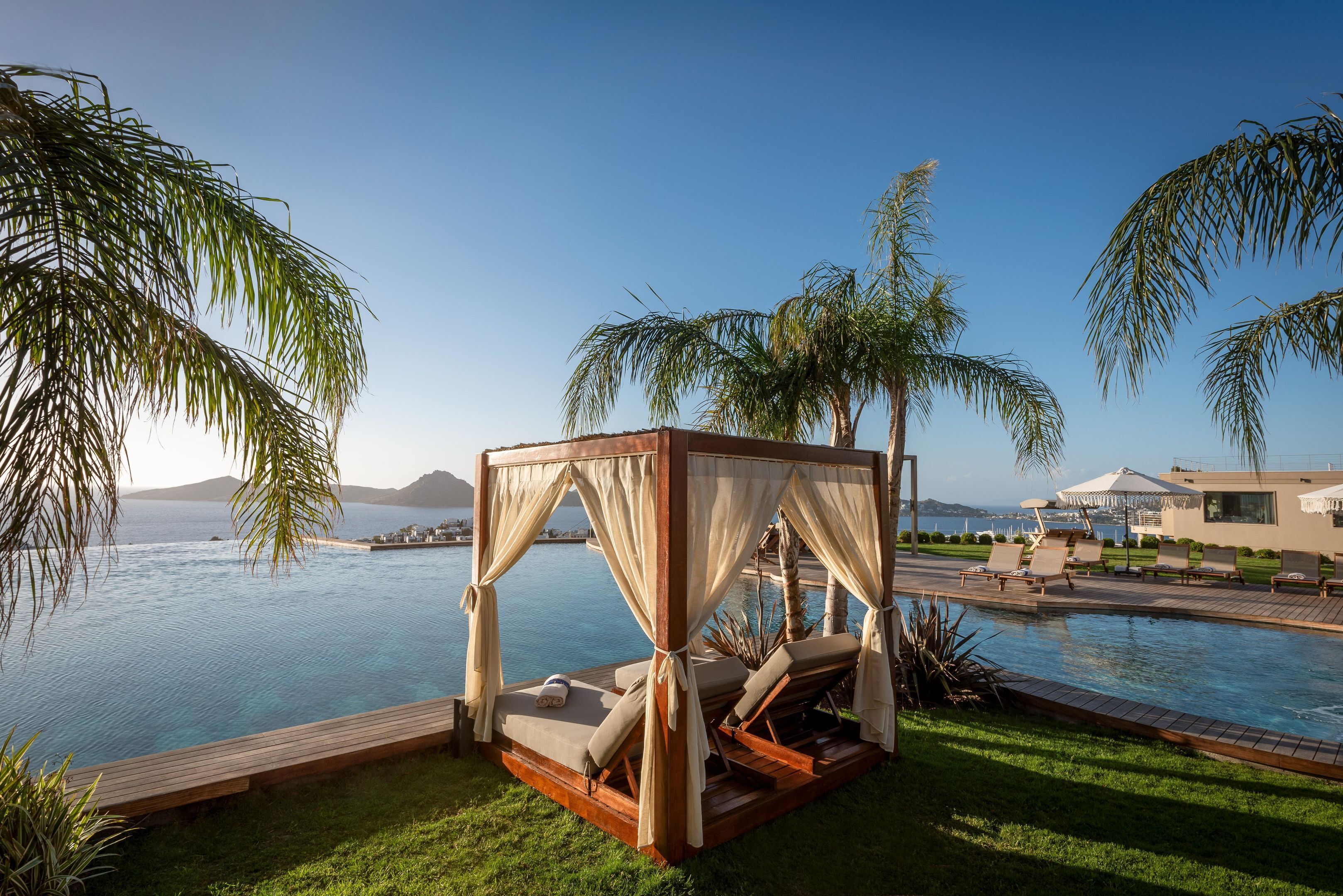 Un espace piscine extérieur luxueux, doté d’une terrasse en bois, d’un lit à baldaquin et de chaises longues.