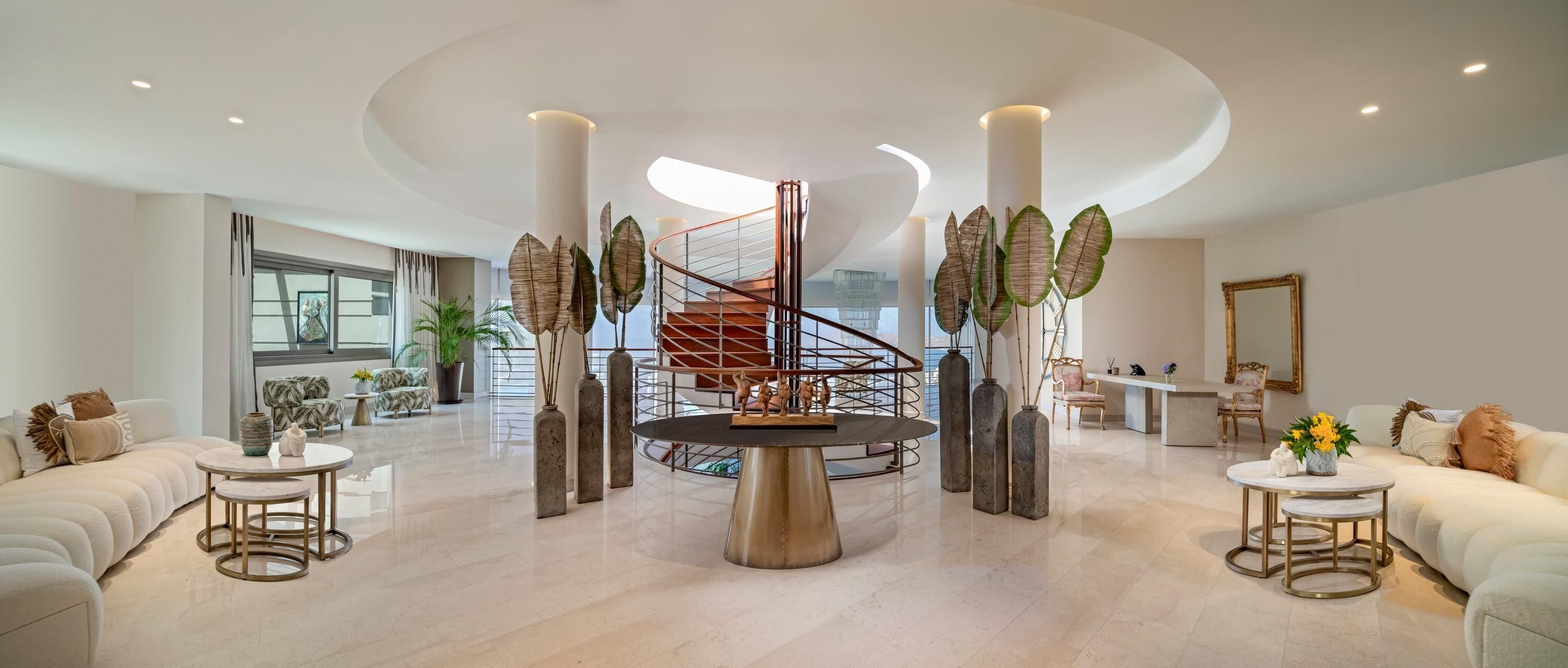 Un amplio vestíbulo con una escalera central, varias zonas de estar y grandes jarrones decorativos.