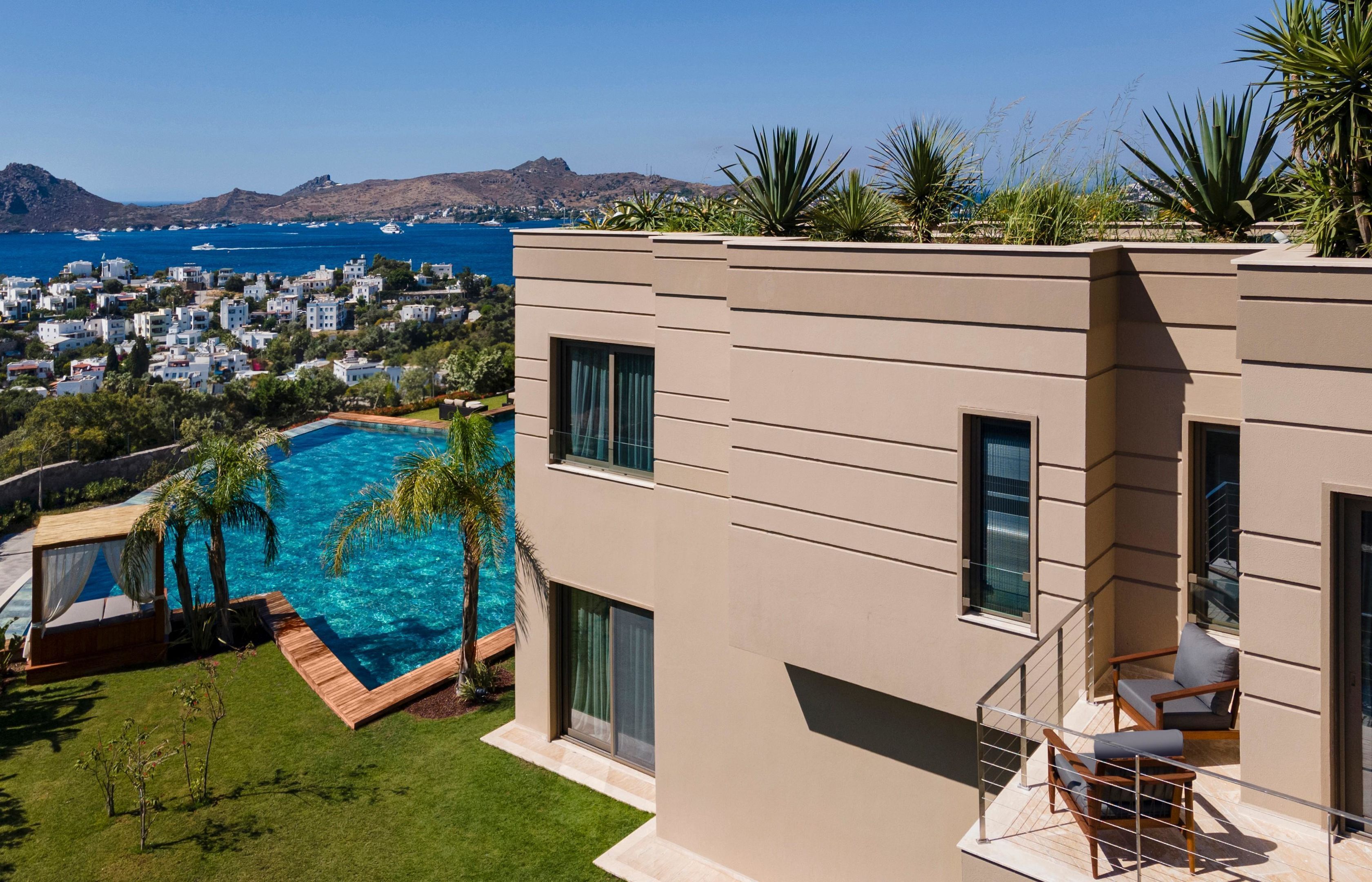 Um edifício moderno com piscina, varanda com assentos e vista para o mar e a cidade.