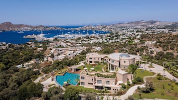 Une villa de luxe dotée d’une piscine, entourée d’une végétation luxuriante et offrant une vue sur la mer et le port de plaisance.
