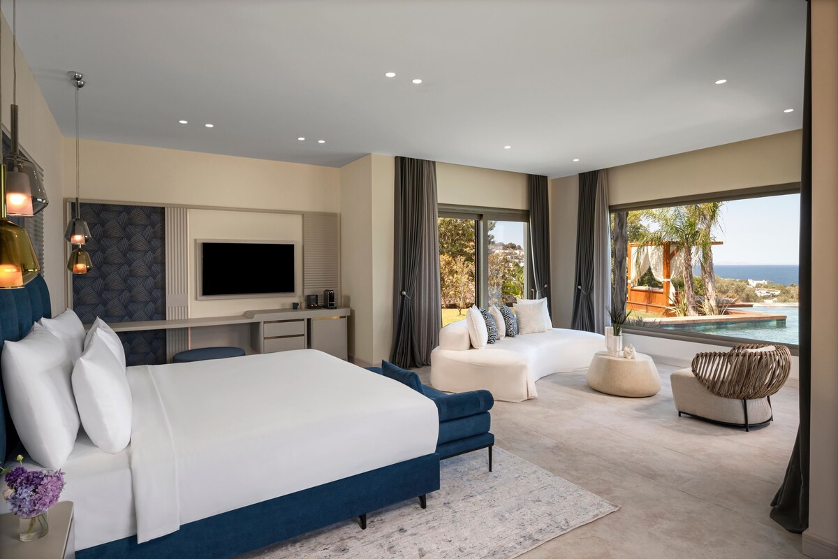 A modern bedroom with a large bed, a TV, and a view of the ocean.