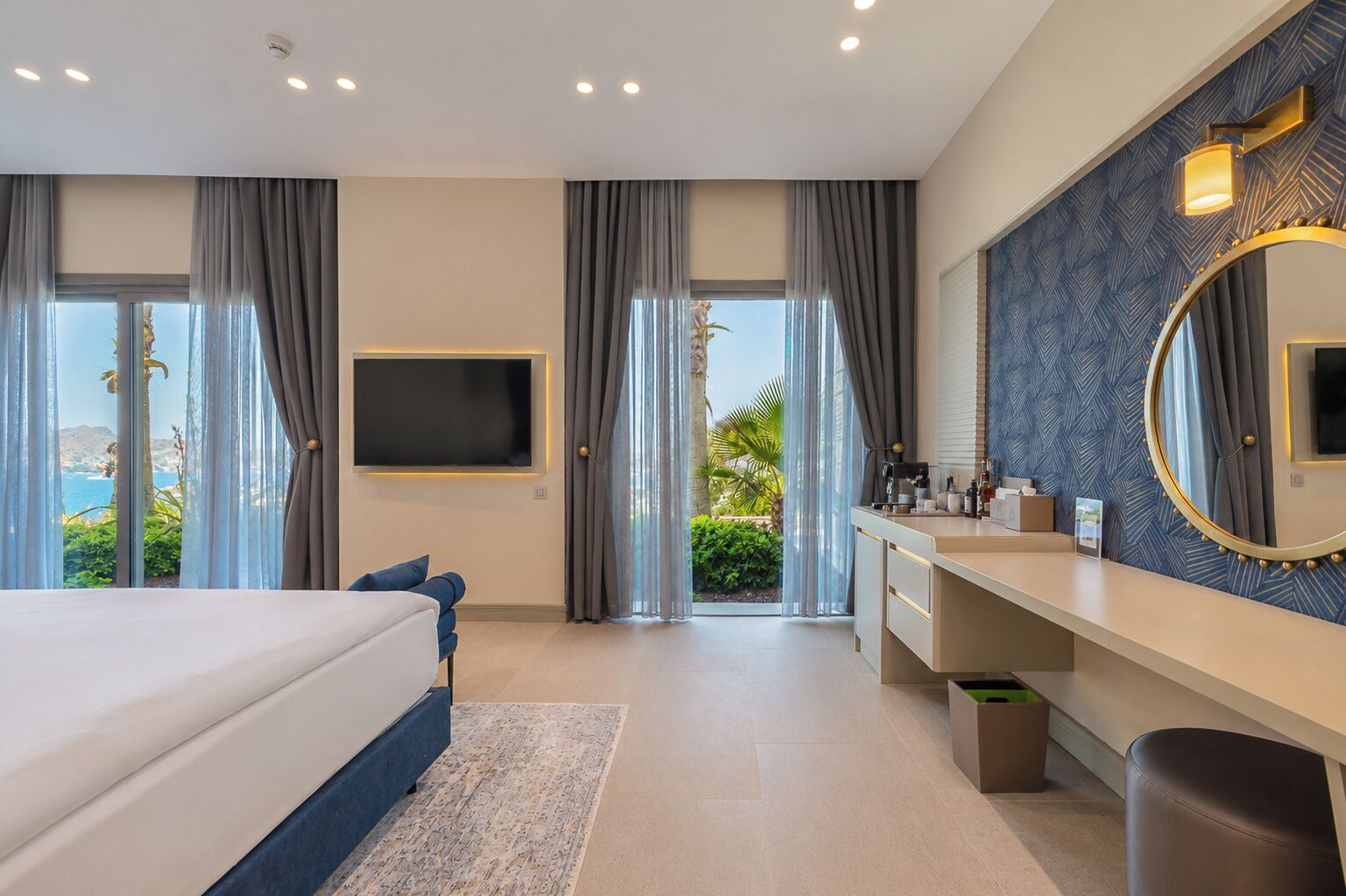 A modern hotel room with a bed, a TV, a bathroom with a mirror, and a view of the outdoors.