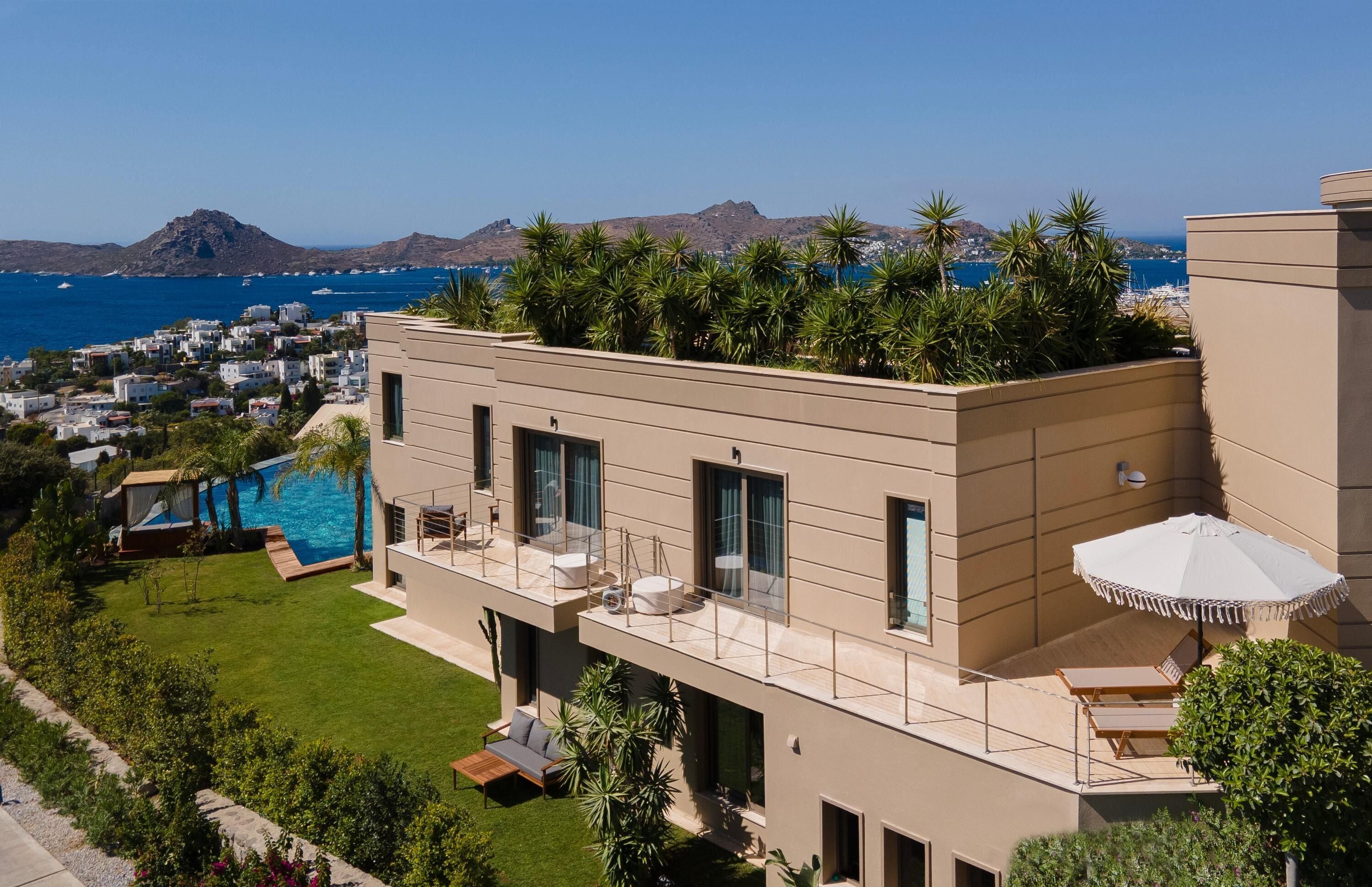 Un edificio moderno de varios pisos con jardín en la azotea, piscina y vistas al mar y a las montañas.