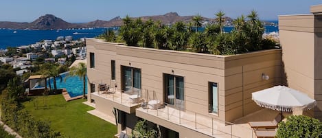A modern multi-story building with a rooftop garden, a swimming pool, and a view of the sea and mountains.