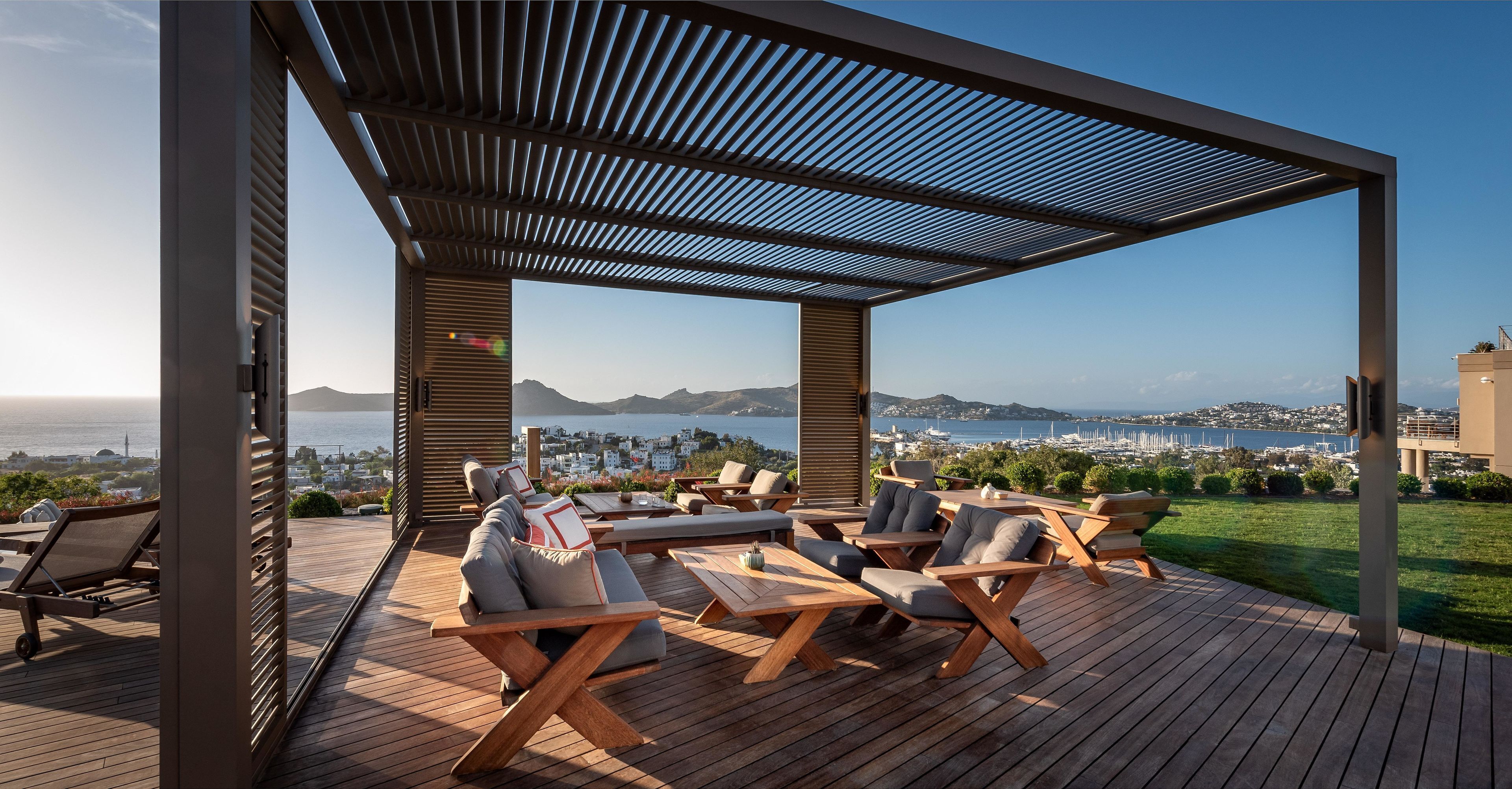 Un espacio de estar al aire libre cubierto con mobiliario de madera y vistas al mar y al paisaje urbano.