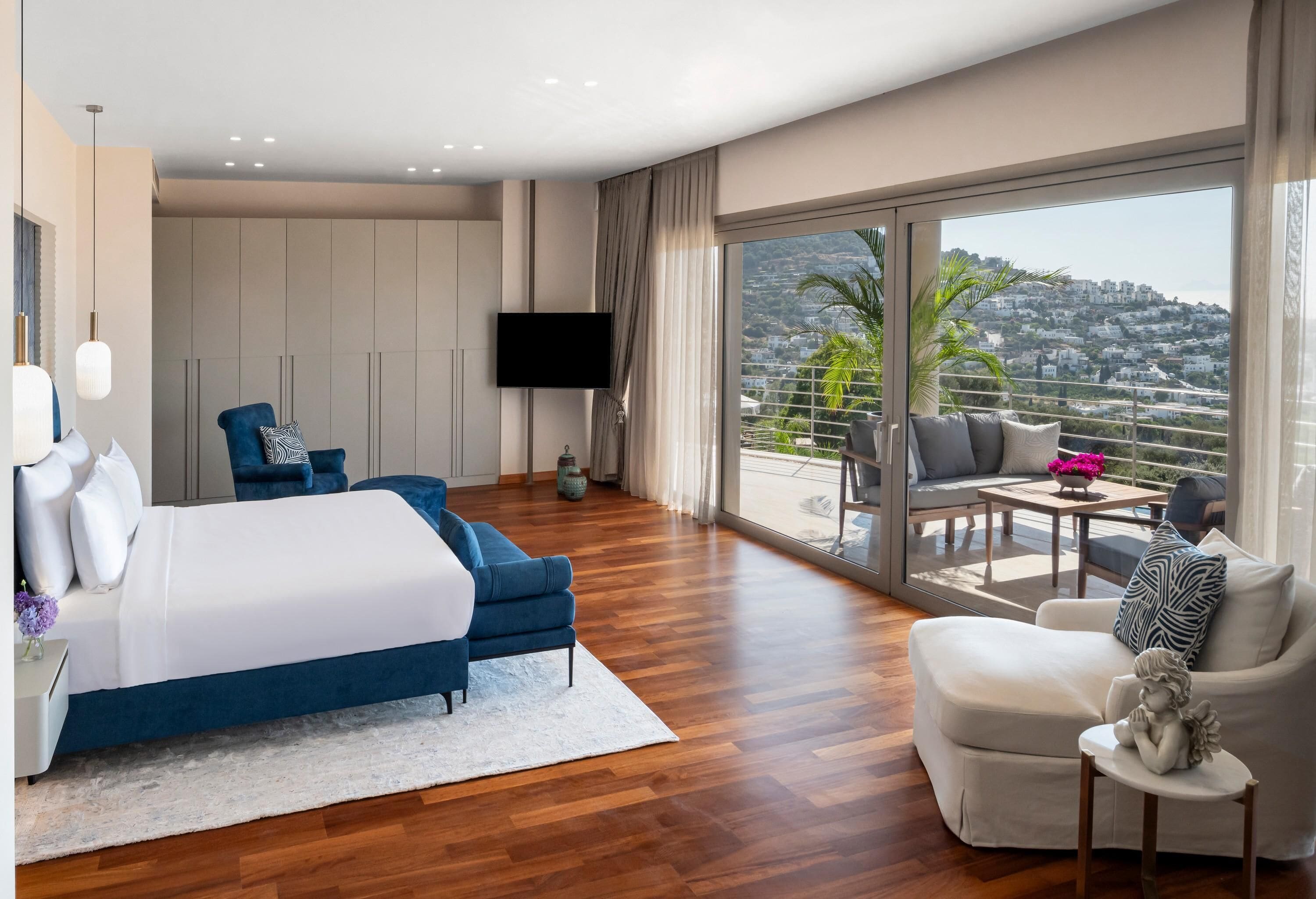 A modern hotel room with a large bed, a sofa, a chair, and a balcony with a view.
