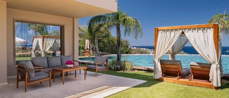 A modern outdoor lounge area with a pool, wooden furniture, and a view of the sea.