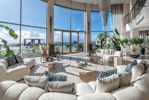 Amplia sala de estar con grandes ventanales, piscina y mobiliario de exterior.