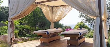 A wooden deck with two massage tables under a canopy.