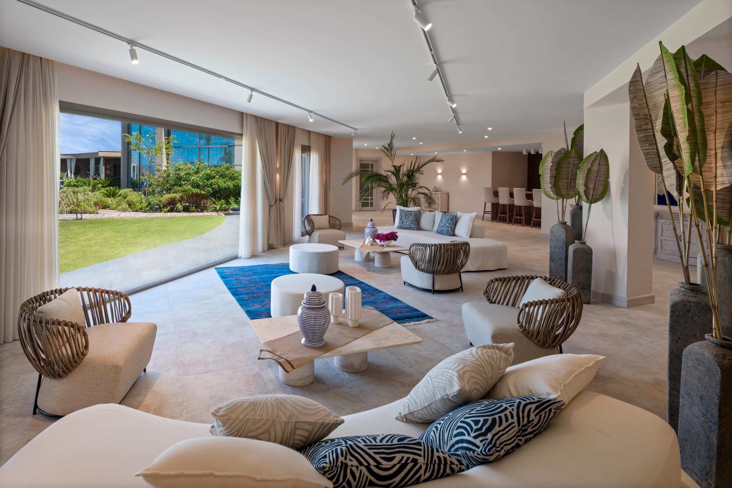 A spacious living room with a large window, a blue rug, and a seating area with a sofa and chairs.