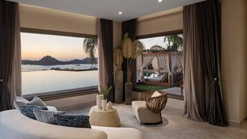 A modern living room with a curved sofa, a round coffee table, and a view of the sea and mountains.