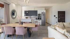 A modern kitchen with a central island, built-in appliances, and a dining area with a wooden table and chairs. - Elia Seaside Deluxe Apartment (Chania)