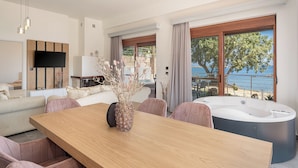 A modern living room with a wooden dining table, seating, a flat-screen TV, and a view of the sea. - Elia Seaside Deluxe Apartment (Chania)