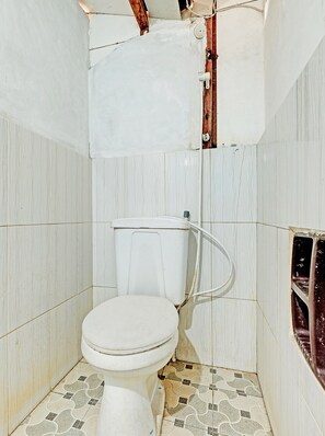 A small, tiled bathroom with a toilet, shower, and a visible electrical outlet on the wall. - SPOT ON 91916 Joglo Doyong Homestay Syariah (Yogyakarta)