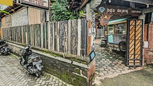 A rustic building with a wooden fence, a motorcycle parked in front, and a small food stall with a blue awning. - SPOT ON 91916 Joglo Doyong Homestay Syariah (Yogyakarta)