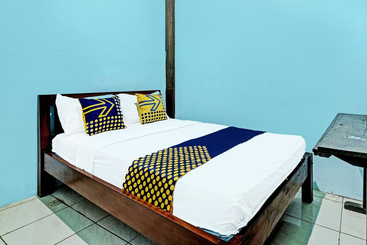 Ein Bett mit weißblauer Bettdecke, zwei Kissen mit blau-gelben Mustern und einem Holz-Kopfteil.