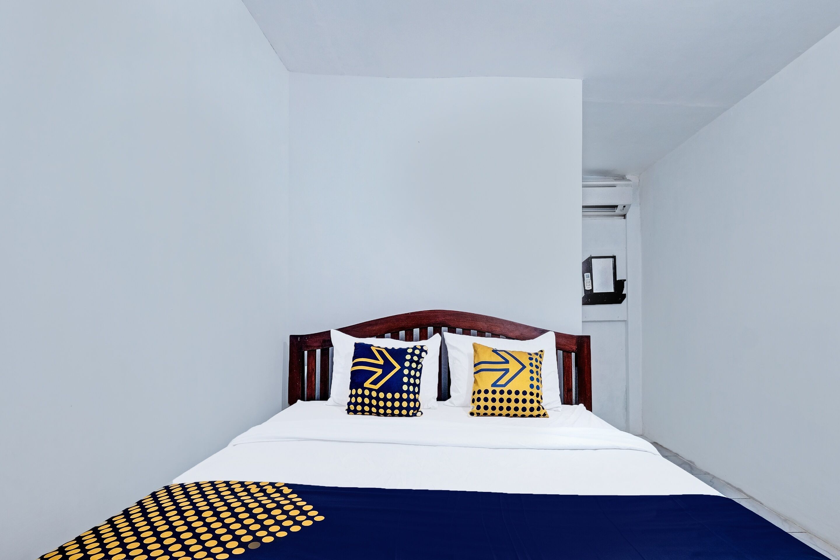 Un dormitorio con cabecera de madera, ropa de cama blanca y almohadas estampadas.