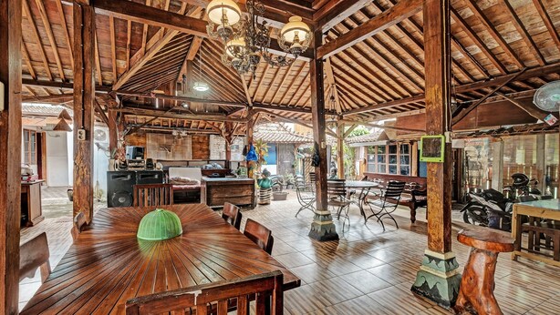 A spacious restaurant with wooden beams, a central dining table, and a ceiling fan. - SPOT ON 91916 Joglo Doyong Homestay Syariah (Yogyakarta)
