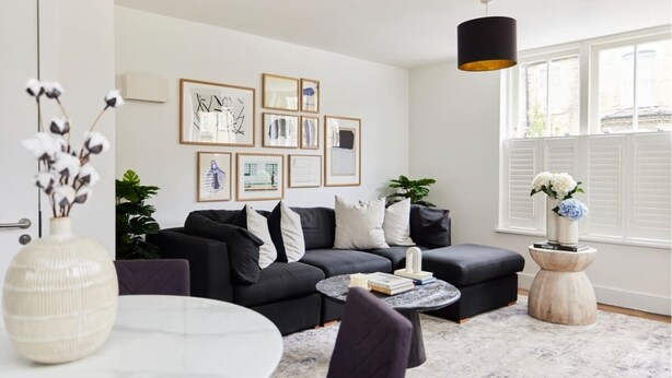 A modern living room with a black sofa, a round coffee table, and framed artwork on the wall. - The Ravenscourt Park Escape - Bright 2bdr Flat (London)