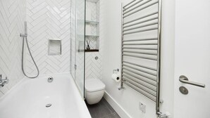 A modern bathroom with a white herringbone tile backsplash, a glass-enclosed shower, a white toilet, and a built-in towel rack. - The Ravenscourt Park Escape - Bright 2bdr Flat (London)