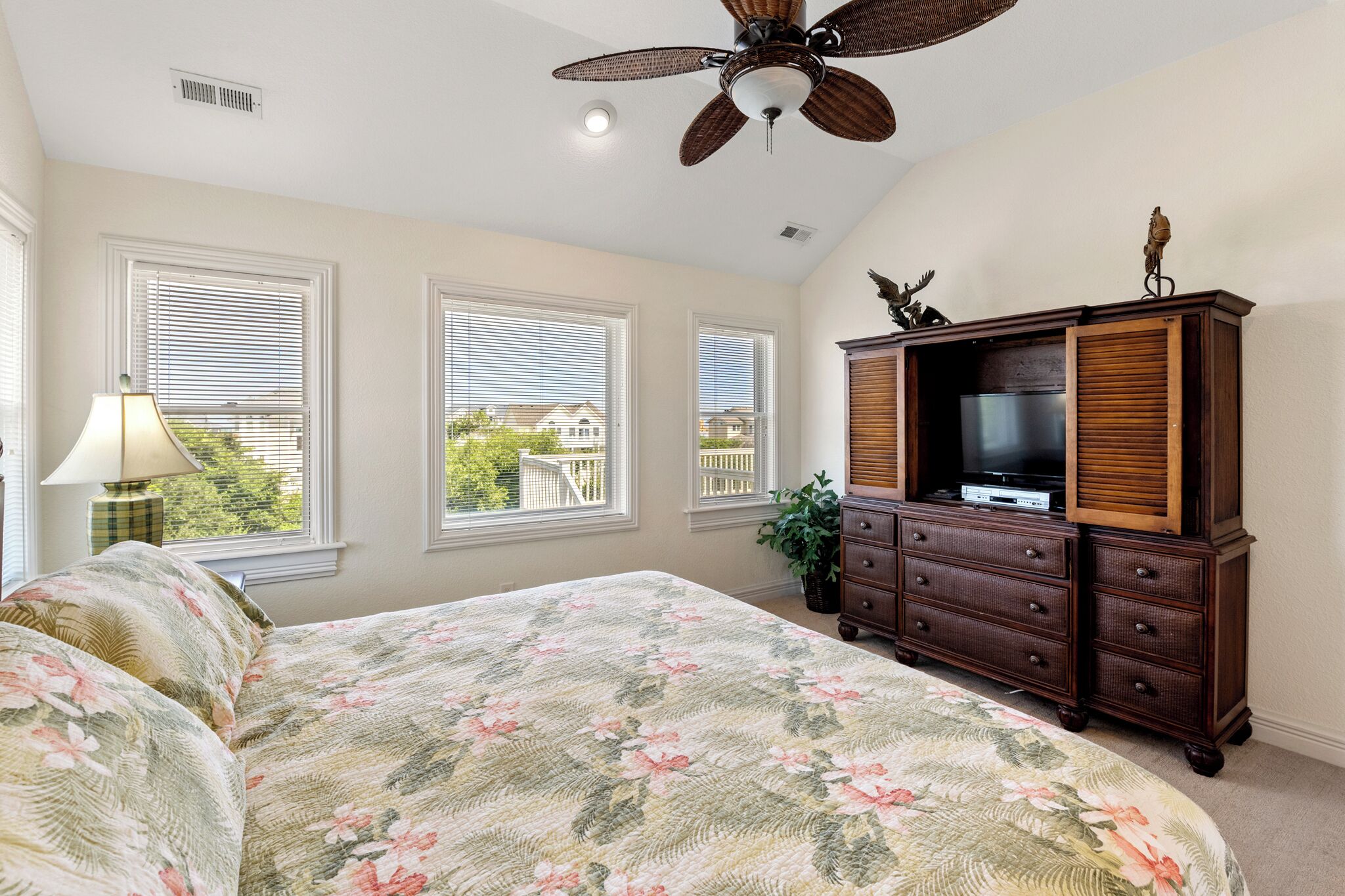 A bedroom with a bed, dresser, TV, and windows with blinds.