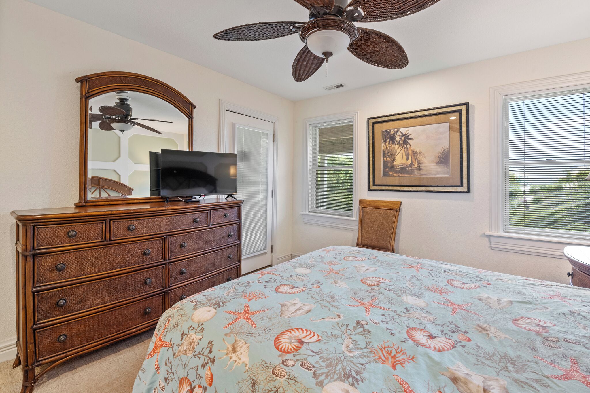 A bedroom with a bed, dresser, ceiling fan, and a framed picture on the wall.