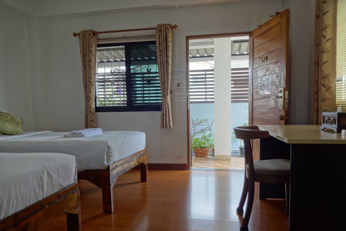 Une chambre d’hôtel avec deux lits en bois, un bureau et une vue sur l’extérieur par une fenêtre munie de rideaux.