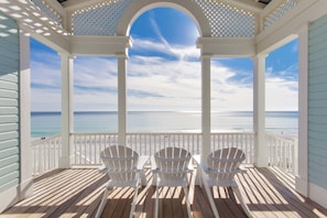 Eine überdachte Terrasse mit weißen Stühlen und Blick auf den Strand.