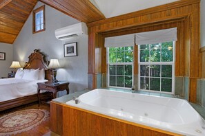 A bedroom with a large bed, a wooden headboard, a window with a view of trees, and a white bathtub. - Swing On Inn I Hot tub, Sleeps 12 (Dripping Springs)