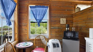 Une pièce de cabane en bois avec une fenêtre, une table et une chaise, un réfrigérateur et un four à micro-ondes.