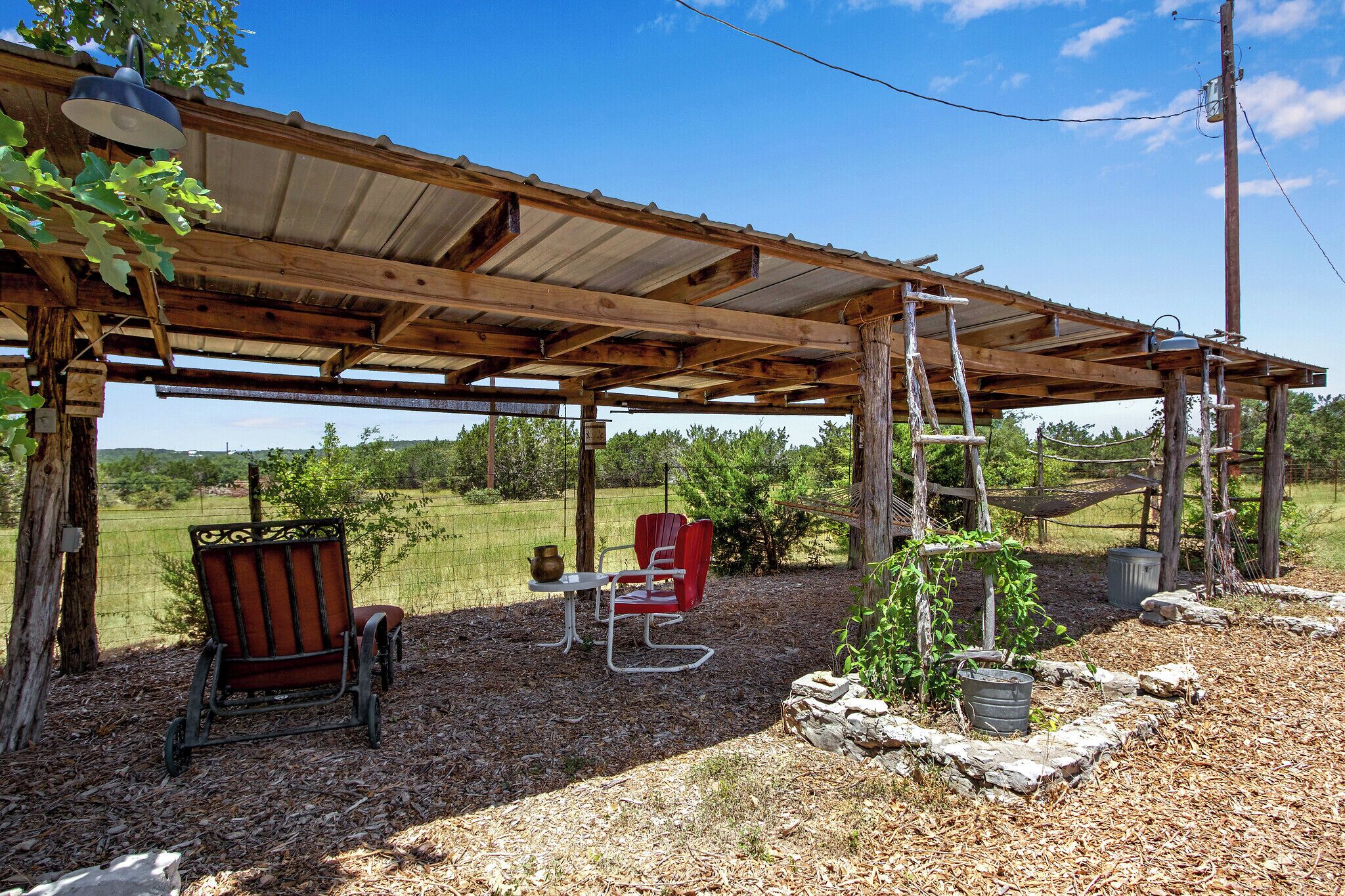 A rustic outdoor seating area with a wooden pergola, a bench, a table, and a red chair.