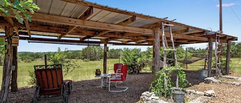 A rustic outdoor seating area with a wooden pergola, a bench, a table, and a red chair.