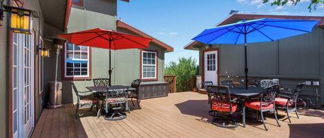 A patio with outdoor furniture and umbrellas, a wooden deck, and a building with a metal roof.