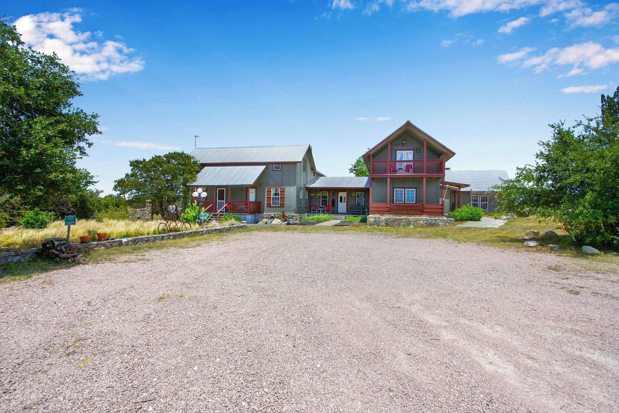 A two-story building with a gravel driveway, a porch, and a stone wall.