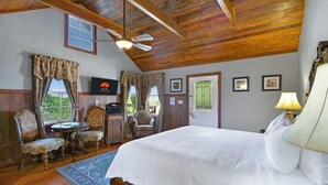 A room with a wooden ceiling, a bed with white bedding, a table with chairs, and a television on the wall.
