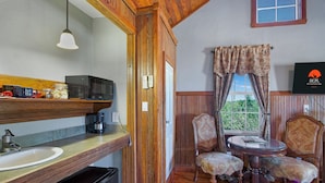 A wooden interior with a kitchen area, a dining table with chairs, and a window with curtains.