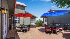 A covered patio with outdoor furniture and umbrellas, a metal trash can, and a wooden deck.