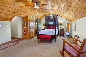 A bedroom with a four-poster bed, a red ottoman, a wooden ceiling fan, and a small bedside table with a lamp. - Swing On Inn - Southern Comfort Suite I Hot tub (Dripping Springs)