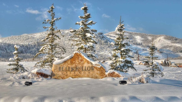 Paisagem coberta de neve com uma placa indicando "BEAR HOLLOW VILLAGE".