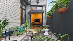An outdoor patio with green metal furniture, a small table with flowers, and hanging planters. - Stunning, Designer Historic Home | Heated Pool (New Orleans)