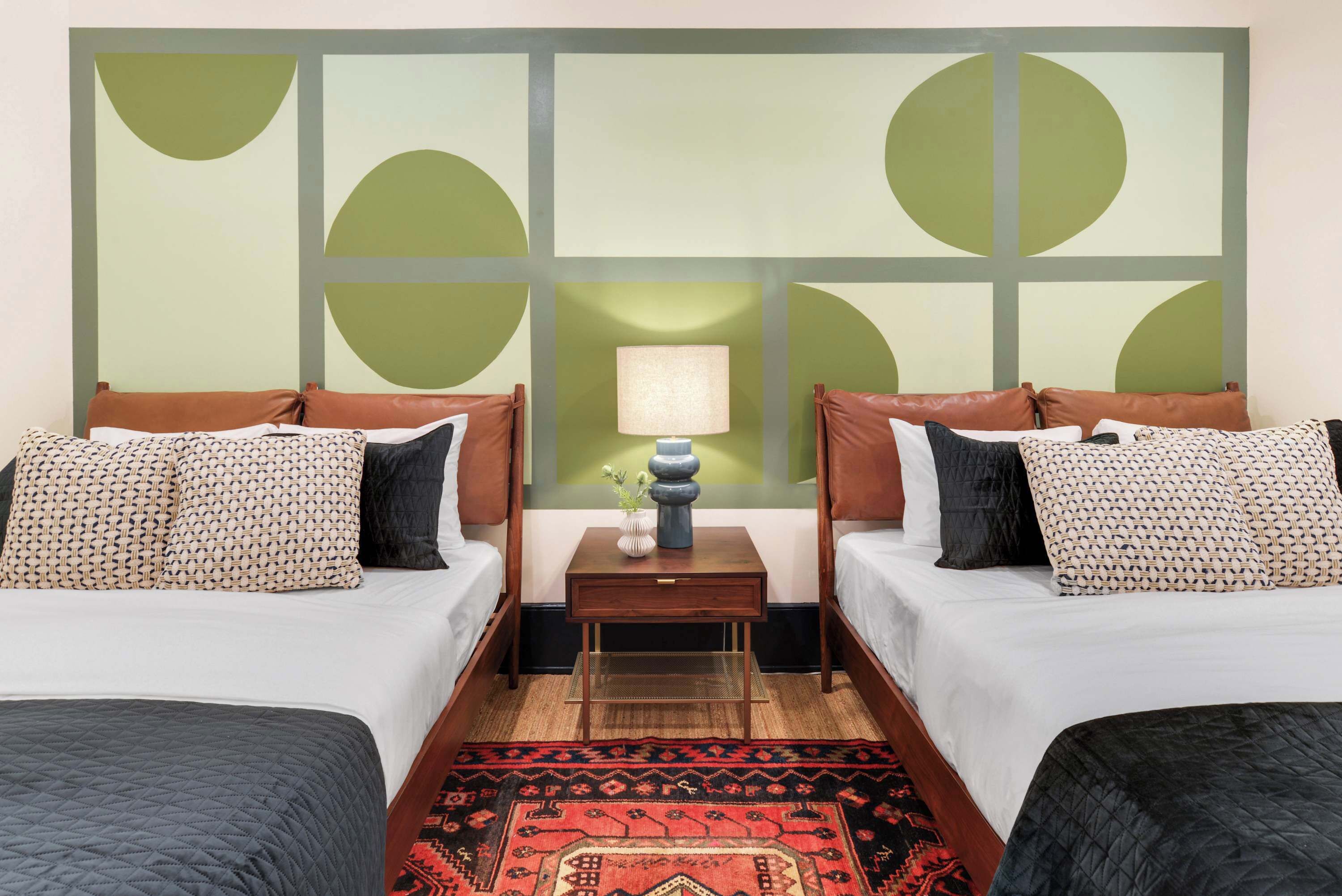 A hotel room with two beds, a nightstand with a lamp, and a decorative wall panel.