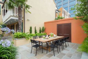 Een terras met een houten tafel en stoelen, omringd door groen en een palmboom.