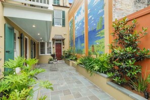 A narrow courtyard with a tiled floor, a red door, and a mural on the wall.