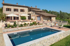A stone house with a swimming pool, outdoor seating, and a garden.